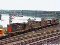 A bit of a hazy Summer day trackside at Bayview Junction finds a westbound CN freight rolling through Bayview Junction with four Geeps as power: CN GP9's 4526, 4595 (still in old green and gold paint), 4475 and 4505. The train is taking the Oakville Sub to CN's Hamilton (Stuart St.) Yard (which can be seen across the bay in the background). The York Street high level bridge at Hamilton Junction is also visible.
<br><br>
<i>Keith Hansen photo, Dan Dell'Unto collection slide (with some colour correction due to a badly faded Ektachrome).</i>