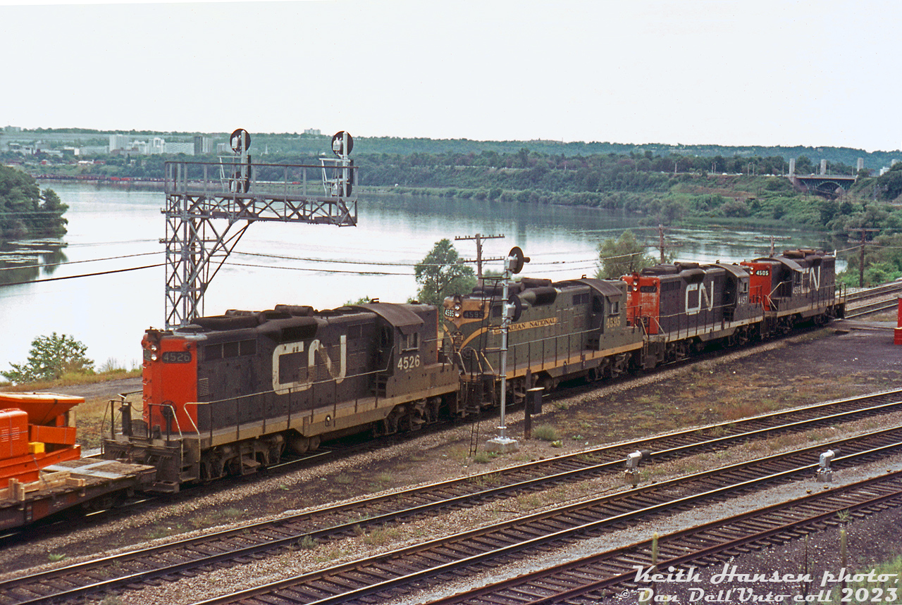 A bit of a hazy Summer day trackside at Bayview Junction finds a westbound CN freight rolling through Bayview Junction with four Geeps as power: CN GP9's 4526, 4595 (still in old green and gold paint), 4475 and 4505. The train is taking the Oakville Sub to CN's Hamilton (Stuart St.) Yard (which can be seen across the bay in the background). The York Street high level bridge at Hamilton Junction is also visible.

Keith Hansen photo, Dan Dell'Unto collection slide (with some colour correction due to a badly faded Ektachrome).