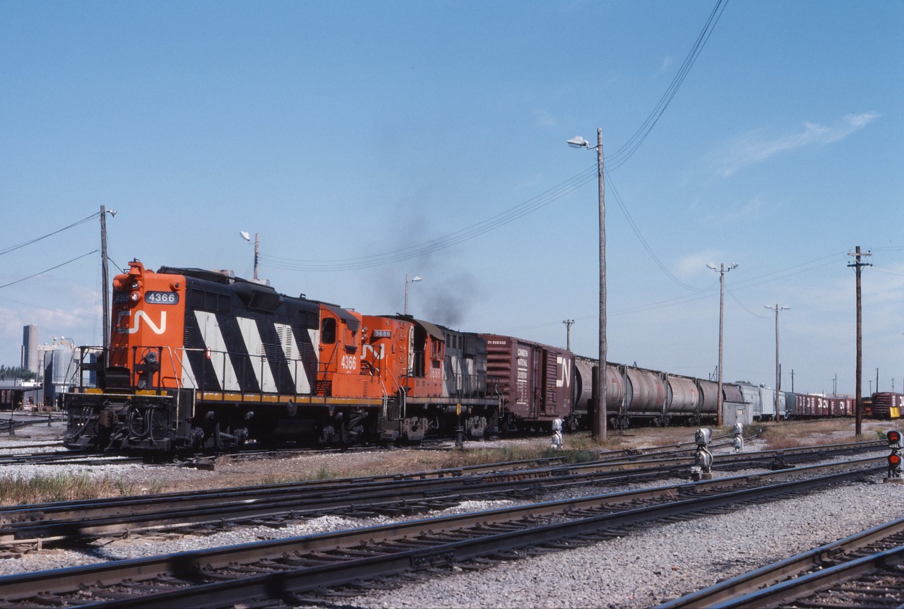 By the mid-1980s, GP9s and RS18s were no longer main line power on CN and CP, often holding down road switcher, transfer, and some yard assignments. On a September Sunday afternoon, CN GP9 4366 (renumbered from 4106 in 1984) and RS18 3668 power a transfer at Pointe St. Charles. In the nearby back shop, GP9s are being rebuilt into slugs or GP9rm--the 4366 would become "slug mother" 7262 in 1990 while the 3688 would be retired but was active into at least 1989.