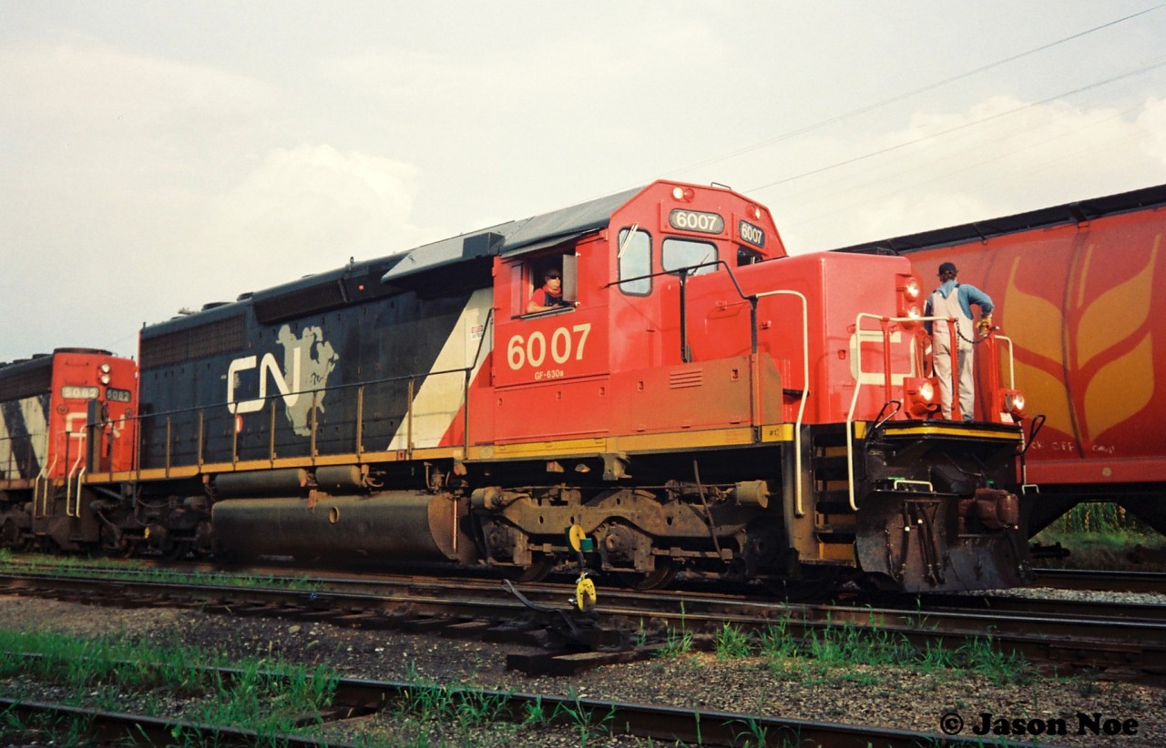 During a hazy summer evening, CN SD40u 6007 and SD40 5082 are the power for train 421 seen performing their work at the Kitchener yard. CN 6007 was released from AMF in Pointe-Saint-Charles, Quebec, fresh from a remanufacturing on April 5, 1993. Also it was the last of the original SD40u 6000-6009 group to be overhauled during a program that had began in 1992. CN 6007 is former CN 5084.