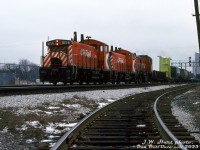<i>Two Pups and a Rocket on the main:</i> CP Rail SW1200RS 8156 and a sister "Pup" team up with an 8000-series RS23 "Rocket" on a westbound extra freight (possibly the London Pickup) rolling over the North Toronto Sub on a gloomy day. The train has just crossed Davenport diamond in the background, and is heading through Osler to hit the West Toronto diamonds before entering the Galt Sub. A dimensional load is visible near the head end: a flatcar hauling an off-highway mining truck dump bed (that appears to be in Terex or Euclid colours).<br><br>In the foreground is the CP "S-Lead" to the old <a href=http://www.railpictures.ca/?attachment_id=38483><b>TG&B Bruce service track</b></a>, that curved south and ran down the east side of the rail corridor parallel to the CN Weston and CP Galt Subs to serve a handful of local industries.<br><br><i>J.W. Hart photo, Dan Dell'Unto collection slide.</i>