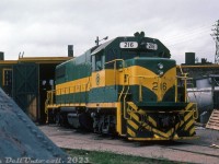 DEVCO Railway 216, a GMD GP38-2, is pictured at their Glace Bay shops partially framed by an old steel wedge plow parked nearby. This unit was part of an order of four units, 216-219, built at GMD London in May-June 1979, and delivered together in early July.
<br><br>
This order was unique in that owner DEVCO (Cape Breton Development Corp) specified these four units be equipped with 575 volt, 1000 kilowatt generators inside them to cover for emergency power outages. The electrical plugs for outputting 3-phase electrical power are visible on the right side of the short hood. The unit survives today as NBSR 2317.
<br><br>
<i>Original photographer unknown, Dan Dell'Unto collection slide.</i>