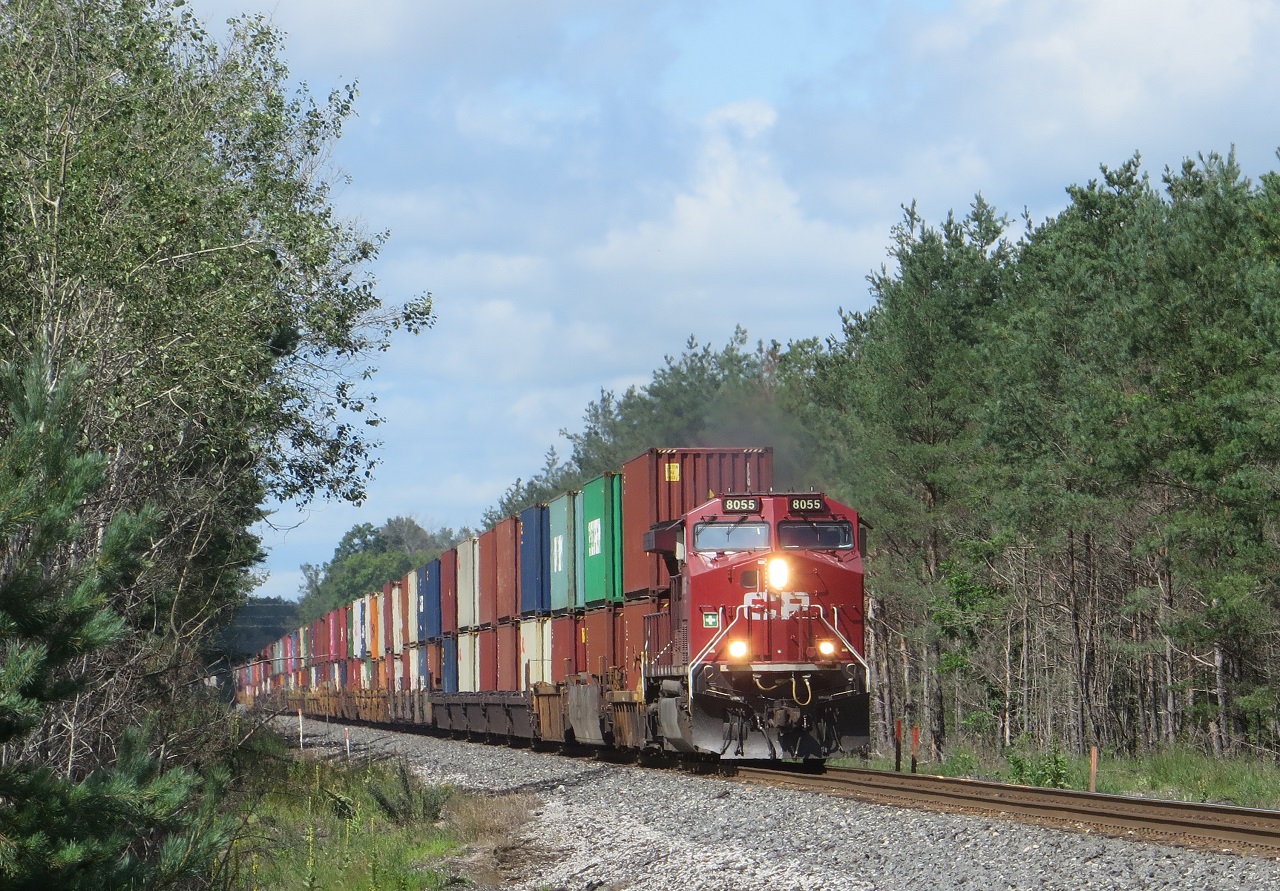 8055 with 8147 mid train is approaching the Highway 26 crossing just north of the former Midhurst station site. The site of the station is now just a patch of grass, but across the tracks a busy  maintenance base remains. A portion of the former passing siding is used as an OCS spur. A huge pile of used ties covers most of the former back track.
