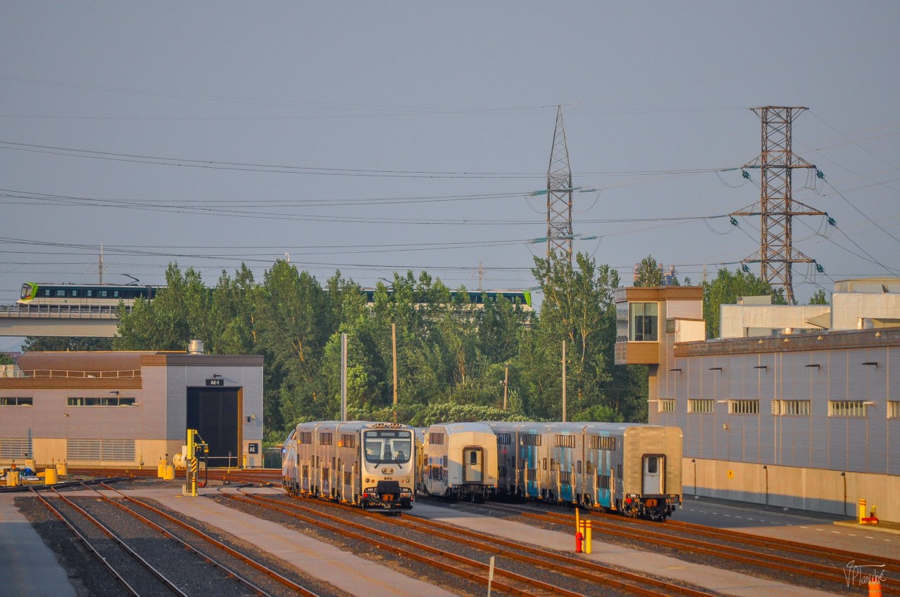 On July 17, 2023, several new EXO cars are parked in the PSC Maintenance Center (EXO side). We see a REM train heading towards Brossard crossing the Pointe-Saint-Charles sector.