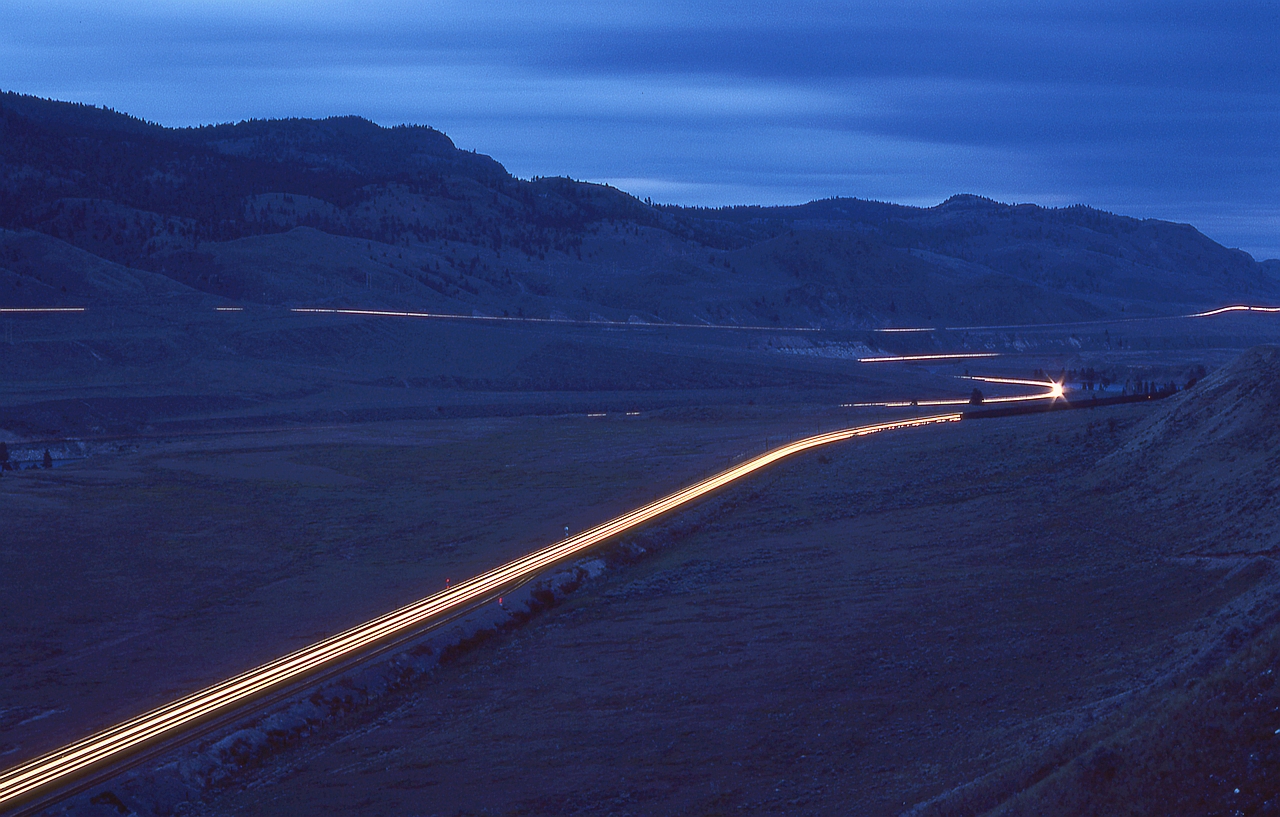 Westward from Kamloops Lake, CP and CN follow the Thompson River into a canyon, through Walhachin and onward to difficult-to-access Semlin (CP on the south side) and McAbee (CN on the north side).  Here is a late evening time exposure eastward view at the east end of CP Semlin on Sunday 1980-06-08, with headlight and ditchlight streaks of CP 5676 + 5651 westbound in the foreground, a CN westbound across the river, and the Trans Canada Highway distant above.  The total peaceful environment there made it a happy campsite for me.