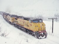 Directly below the Saddle Rock Tunnel on the Trans Canada Highway in the Fraser Canyon, a CP grain train with three UP Dash8-41CW units on loan for evaluating possible General Electric locomotive purchases (which eventually occurred in 1995) is experiencing winter snow as they leave Saddle Rock at 1503 PST on 1991-03-03 headed for Yale and onward to the CP yard in Port Coquitlam.

<p>A slightly later view posted a while back is at <http://www.railpictures.ca/?attachment_id=45854>.