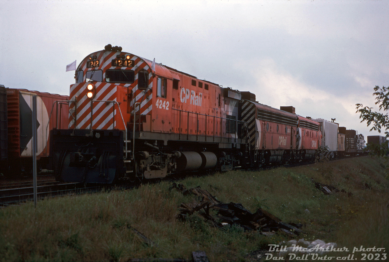 A westbound CP Rail extra freight waits at Galt in the evening (exact spot unsure) lead by an eclectic gathering of power: CP C424 4242, F7B 4434 and FP7 4031. One of CP's many wooden vans (caboose) is curiously marshalled two cars back, mingling with the mixed freight.

Each unit here had some significance on the roster: CP C424 4242 was one of the first two units (along with C424 4239) painted in the new "CP Rail" 1968 multimark livery, and ran on the publicity train of matching multi-coloured freight cars often seen on postcards.

CP F7B 4434 was formerly numbered 1908 (originally renumbered from 4434 to 1908 in the mid-1950's for use on CP's new transcontinental train "The Canadian"), and the only F7B to get action red as a 1900-series unit (it wasn't renumbered back to the 4400's with the other F7B's until later).

CP FP7 4031 acquired its trademark drooping rear end or "hunchback" after trailing one of the two trains involved in a fatal head-on collision in Bowden AB in April 1971. Despite being the trailing unit, its nose was damaged when the loaded grain boxcar behind rammed into it, and was repaired with the nose of sister unit 4039 (also involved in the wreck). The collision damaged 4031's frame (hence the drooping rear end), but the unit was otherwise repaired and served for many years after in this state.

Bill McArthur photo, Dan Dell'Unto collection slide.
