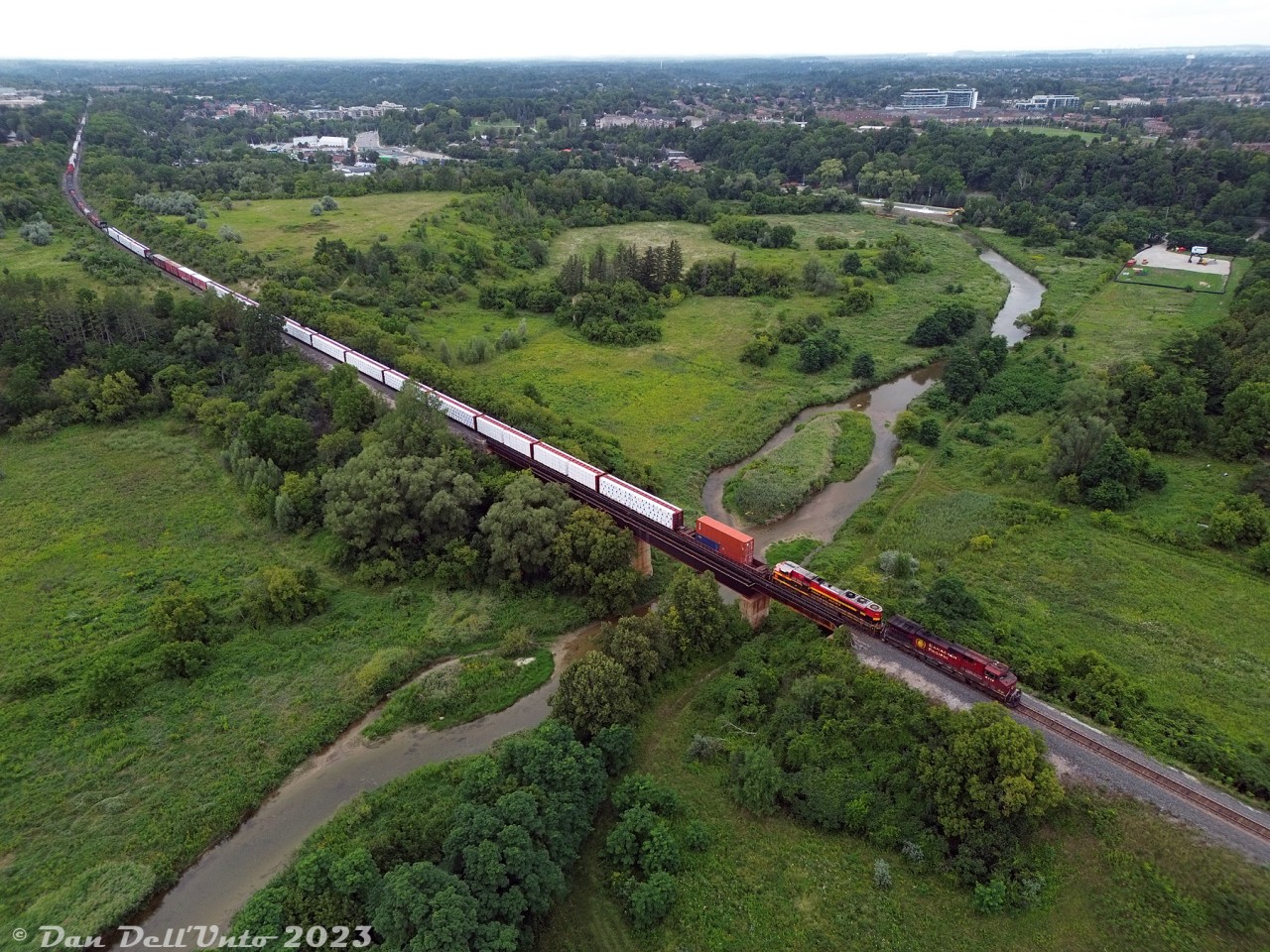 CPKC train #420 makes its way south down the MacTier Sub, crossing the mighty Humber River south of Woodbridge on the approach to Emery. Today's power is CP AC4400CW 9713 and KCSM SD70ACe 4163.

CP's Humber River bridge at Mile 10.48 MacTier Sub was constructed as part of one of the old line realignments around Woodbridge: the original Toronto, Grey & Bruce line snaked through the lower part of the valley here and crossed the river at a lower bridge*, until straightening and elevating the line for the present high-level bridge shown. The original TG&B line at the upper left also kept going straight off to the left (to out of frame) at the present curve, once entering Woodbridge on a more westerly alignment. This was realigned east to the present alignment (north of the curve, heading into the distance) around 1907-1908, and the north end of the old alignment became a short spur into town.

And if that wasn't enough, the old Toronto Suburban Railway interurban line from Weston to Woodbridge snaked along the Humber River through the valley here until its discontinuance in 1926. (A look at some old aerial imagery from 1961 shows a few of the old alignments from both.

* That small white square, visible poking up in the Humber River north of the "island" on the east side, may be an old bridge abutment from the original alignment.
