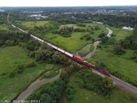 CPKC train #420 makes its way south down the MacTier Sub, crossing the mighty Humber River south of Woodbridge on the approach to Emery. Today's power is CP AC4400CW 9713 and KCSM SD70ACe 4163.
<br><br>
CP's Humber River bridge at Mile 10.48 MacTier Sub was constructed as part of one of the old line realignments around Woodbridge: the original Toronto, Grey & Bruce line snaked through the lower part of the valley here and crossed the river at a lower bridge*, until straightening and elevating the line for the present high-level bridge shown. The original TG&B line at the upper left also kept going straight off to the left (to out of frame) at the present curve, once entering Woodbridge on a more westerly alignment. This was realigned east to the present alignment (north of the curve, heading into the distance) around 1907-1908, and the north end of the old alignment became a short spur into town.
<br><br>
And if that wasn't enough, the old Toronto Suburban Railway interurban line from Weston to Woodbridge snaked along the Humber River through the valley here until its discontinuance in 1926. (A look at some old <a href=https://www.toronto.ca/ext/archives/s0012/fl1961/s0012_fl1961_it0271.jpg><b>aerial imagery from 1961</b></a> shows a few of the old alignments from both.
<br><br>
<i>* That small white square, visible poking up in the Humber River north of the "island" on the east side, may be an old bridge abutment from the original alignment.</i>