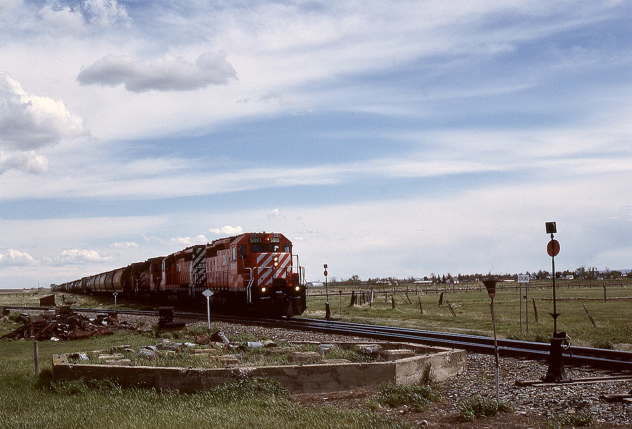 CP’s Montana subdivision runs generally southwest from the Lethbridge area to a BNSF interchange at Coutts/Sweetgrass, with two junctions at Stirling.  The nearer switchstand is for the Stirling sub. seen exiting to the left, and the farther one is for the Cardston sub. visible exiting to the right, as a Coutts Turn with 5810 + 5801 + 5759 + 5813 passes the old water tower foundation heading for Lethbridge on Friday 1989-05-26 at 1522 MDT.

Nowadays, the Stirling sub. is only a spur, reaching 49 miles eastward to Foremost, and the Cardston sub. is disconnected right at Stirling per https://maps.app.goo.gl/j52QTLsaV2Hv8oUu5?g_st=im.