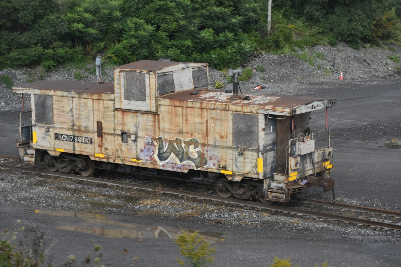 Battered and boarded up CN 79834 sits at Pointe St. Charles, QC waiting for its next assignment as a rider car.