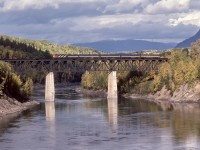 Westward from Smithers, CN’s northern mainline to Prince Rupert follows first the Bulkley River to Hazelton then the Skeena River most of the way to the Pacific Ocean, crossing that river once, just west of the aptly named flagstop of Skeena Crossing.  Here is train number 9, VIA’s Skeena (nicknamed the Rupert Rocket), on that steel deck truss bridge at mileage 62.3, with CN 9158 leading the VIA consist (with a CN business car carrying the markers) on Thursday 1979-10-04, as seen from the north riverbank.