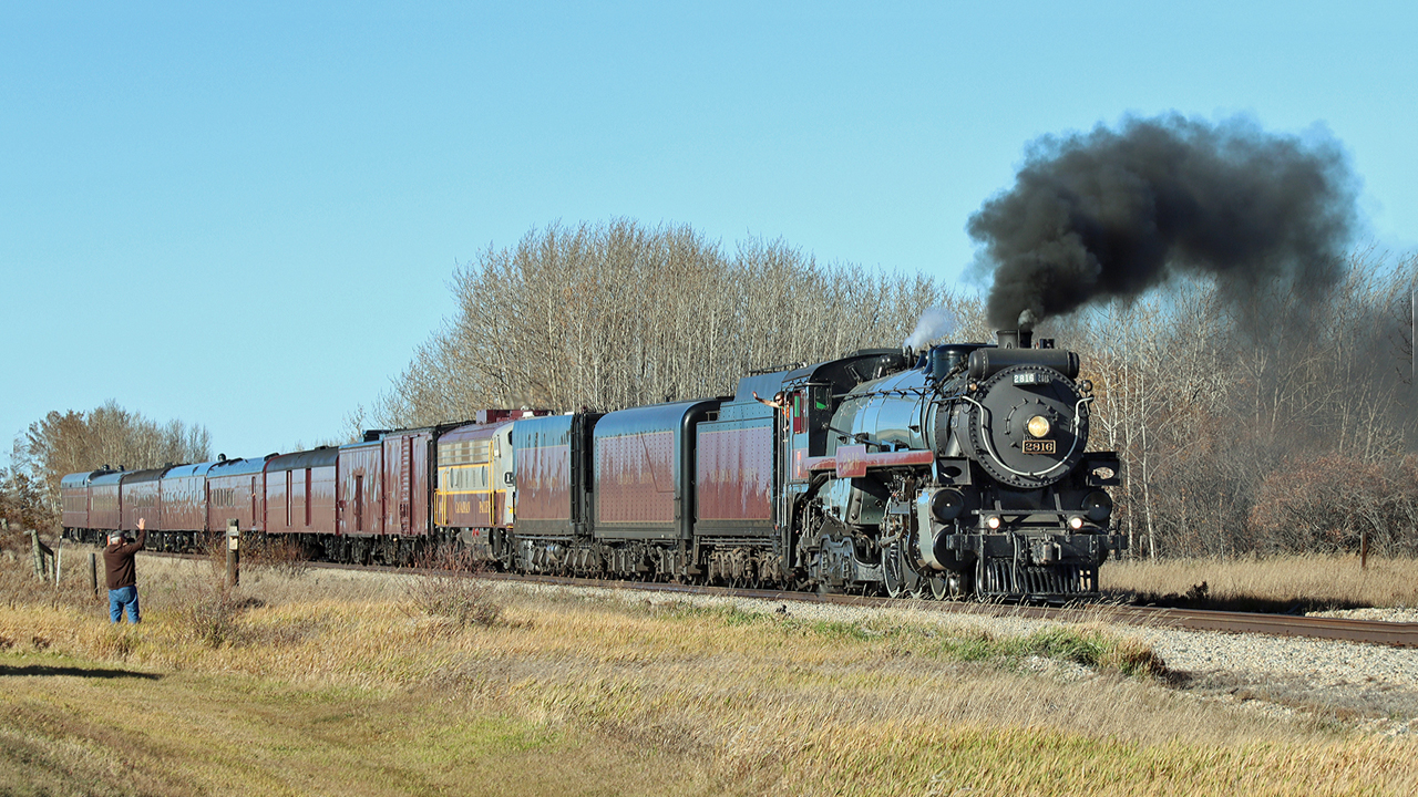 CPKC's steam engine 2816, with it's heritage train set,  makes it's way south on the Red Deer sub, with a friendly wave from one of the crew.