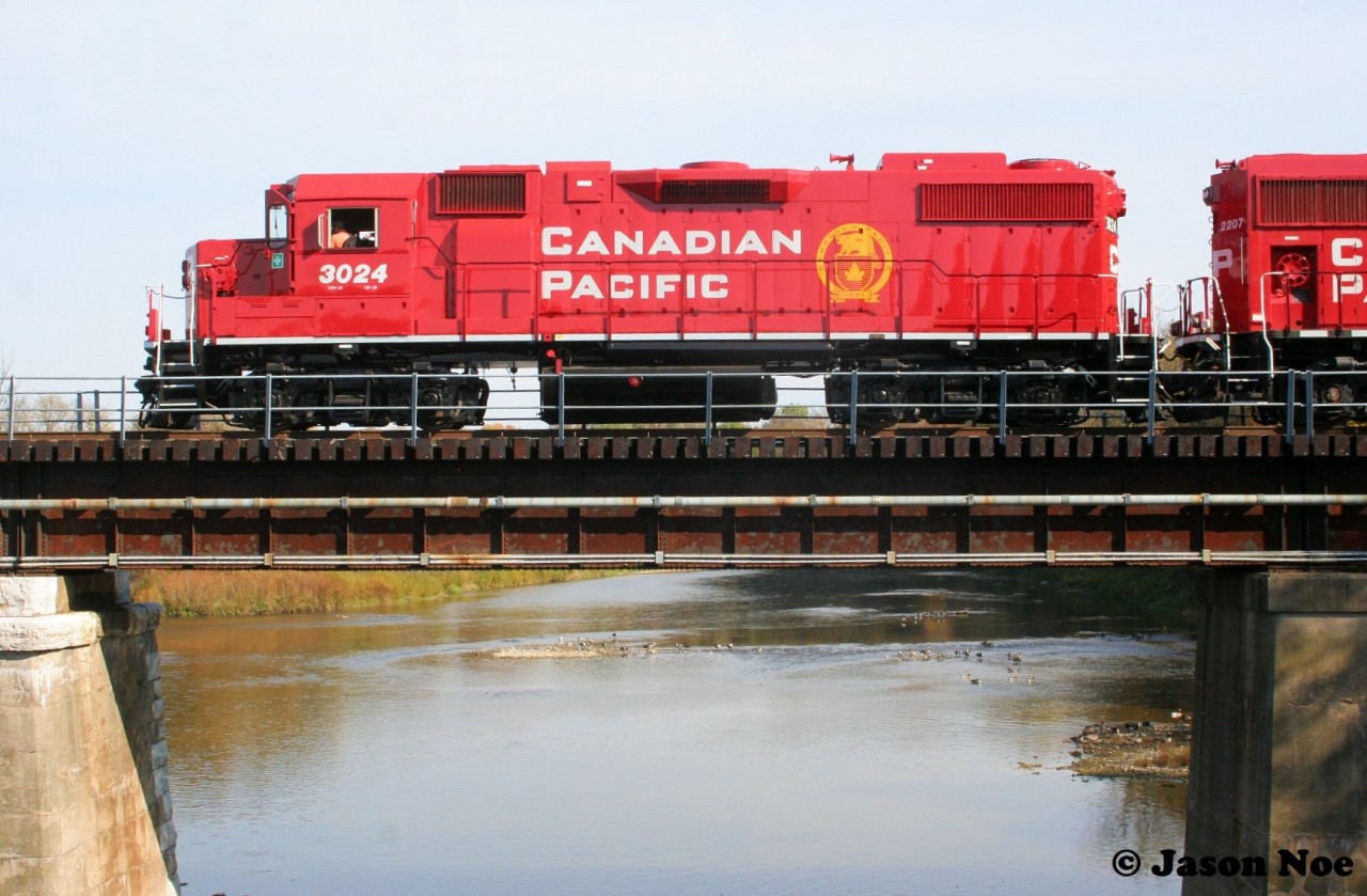 In April of this year both Canadian Pacific and Kansas City Southern came together to form CPKC. Over half a year later and locomotives are still being repainted in Canadian Pacific colors with the beaver shield logo. 

Here, the crew of CPKC H70 have the best view in the house as they pause over the Grand River in Kitchener, Ontario on the Waterloo Subdivision. The consist included CP 3024 and 2207, with GP38-2 3024 having recently been repainted in a fresh coat of red at the Progress Rail facility in Mayfield, Kentucky.