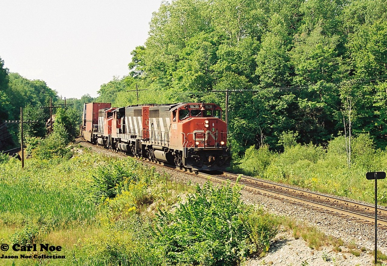 During a summer afternoon, a southbound CN train with 9638, 9554 and 9403 is approaching the crossing at Rosseau Road, which is south of Parry Sound, Ontario on CN’s Bala Subdivision.