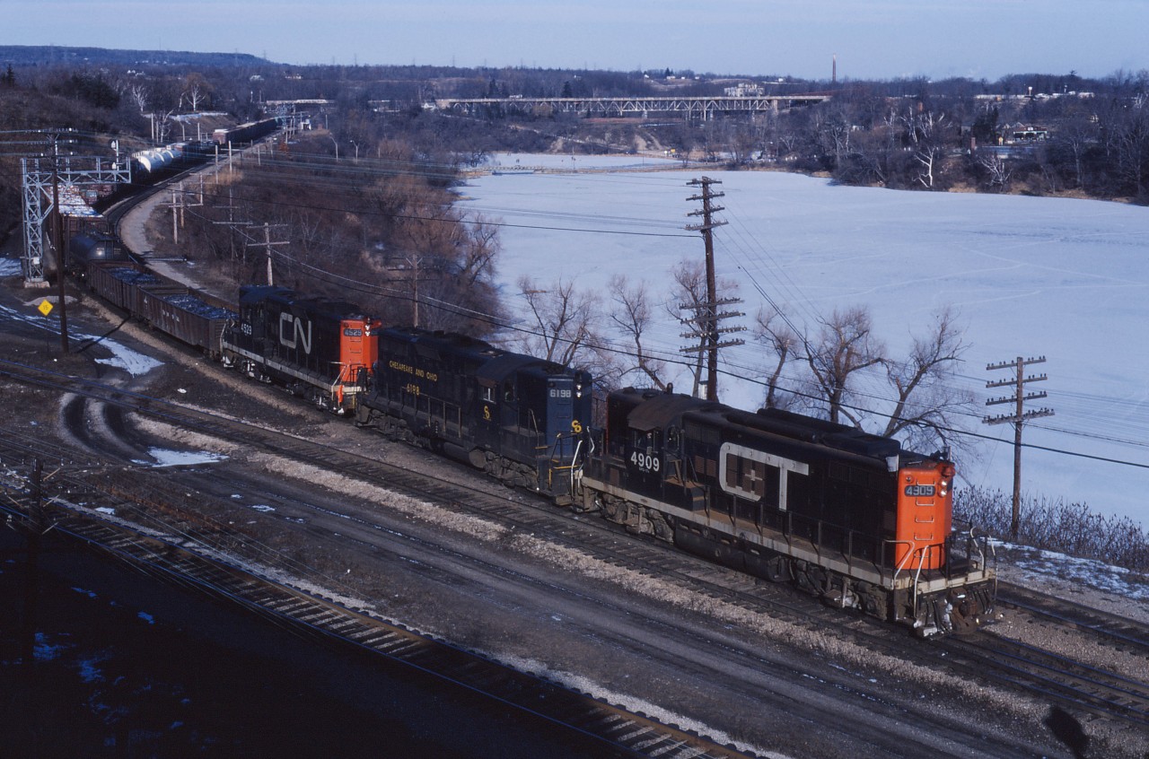 Leased power leads a westbound around the bay at Hamilton Junction on a cold but bright winter day. According to UCRS Newsletters, in January of 1973, CN had 11 geeps on lease from its GTW subsidiary and 45 GP9s from the C&O. Delivery of new 5500 series GP38-2s had commenced at the beginning of December and the GTW units will returned home in January and March 1973. Some of the C&O GP9s will stay on lease into early 1974. (For the record, power is GP9s GTW 4909, C&O 6198, and CN 4529.)
