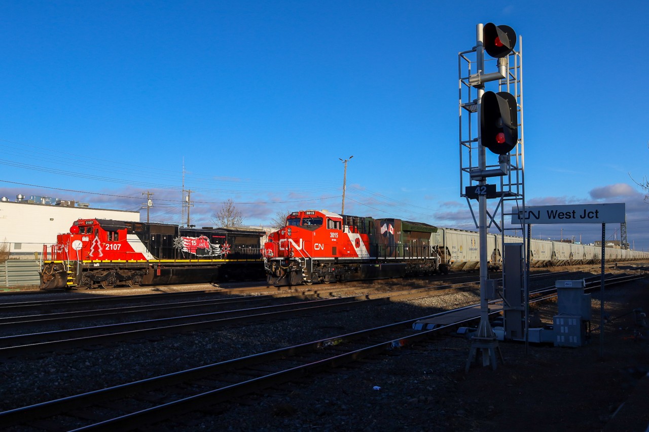 G 81141 25 rolls through West Junction with CN 3015 leading.  Parked at the diesel shop, is the power for the CN Christmas Express, which consists of CN 2107 and CN 2112, both sporting the 15 year IPO anniversary scheme.