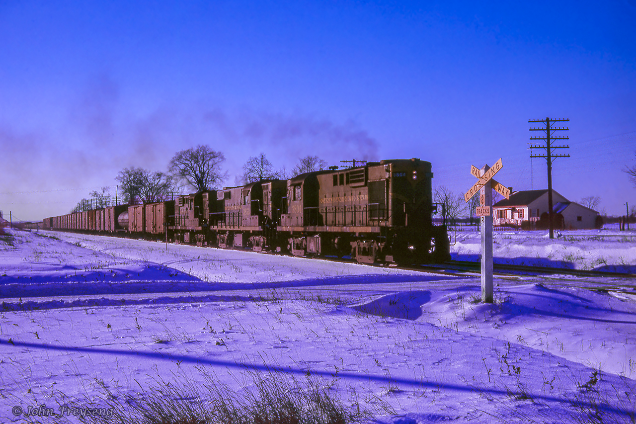 Approaching the western yard limits of Belleville, an eastbound CN freight from Mimico for Montreal makes its way across the snowy countryside of eastern Ontario.Scan and editing by Jacob Patterson.