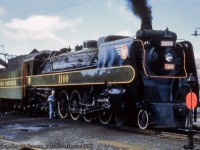 Built in 1936 by CLC Kingston, one of ONR's four 4-8-4 Northern locomotives (1100 - 1103) takes on water and receives some attention from the engineer during a passenger stop. The largest of ONR's steam power, these were typically assigned to the 'Northland' passenger train between North Bay and Cochrane, but also appeared in the Toronto area on lease to CNR.  None have been preserved.<br><br>No information was provided with this slide regarding date, location, or photographer, however Cochrane is a guess due to proximity to the street, and based on other images of the station, there were tracks on the north side of the station. The only bit of information seen beyond the locomotive is a sign appearing to partially read, "Minnawas..." The running board along the locomotive is the later, thicker stripe, rather than the original thin one seen <a href=http://www.trainweb.org/oldtimetrains/photos/onr/1100_quintland.jpg>in this 1939 image.</a>  Any further information would be appreciated.<br><br><i>Original Photographer Unknown, Jacob Patterson Collection Slide.</i>