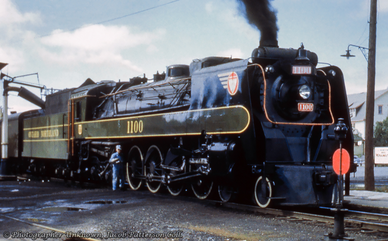 Built in 1936 by CLC Kingston, one of ONR's four 4-8-4 Northern locomotives (1100 - 1103) takes on water and receives some attention from the engineer during a passenger stop. The largest of ONR's steam power, these were typically assigned to the 'Northland' passenger train between North Bay and Cochrane, but also appeared in the Toronto area on lease to CNR.  None have been preserved.No information was provided with this slide regarding date, location, or photographer, however Cochrane is a guess due to proximity to the street, and based on other images of the station, there were tracks on the north side of the station. The only bit of information seen beyond the locomotive is a sign appearing to partially read, "Minnawas..." The running board along the locomotive is the later, thicker stripe, rather than the original thin one seen in this 1939 image.  Any further information would be appreciated.Original Photographer Unknown, Jacob Patterson Collection Slide.
