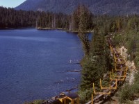 On northern Vancouver Island, Canadian Forest Products had a spur eastward from Woss to a road-to-rail log reload at Crowman Lake (which CFP spelled Croman), passing along the north side of Hoomak Lake around the halfway mark, thus the H-Line name of that spur.  On Wednesday 1979-08-29, dynamic-brake-equipped SW1200 301, new to CFP in 1956, handled a long string of skeleton log empties by Hoomak Lake enroute the Croman reload, with Mount Markusen prominent in the background.

<p>This H-line spur is the same line where a multiple-fatality runaway of loaded log cars occurred closer to Woss on 2017-04-20 (https://www.tsb.gc.ca/eng/rapports-reports/rail/2017/r17v0096/r17v0096.html) which resulted in the total shutdown of that railway (then the Englewood Railway of Western Forest Products) as announced on 2017-11-07.