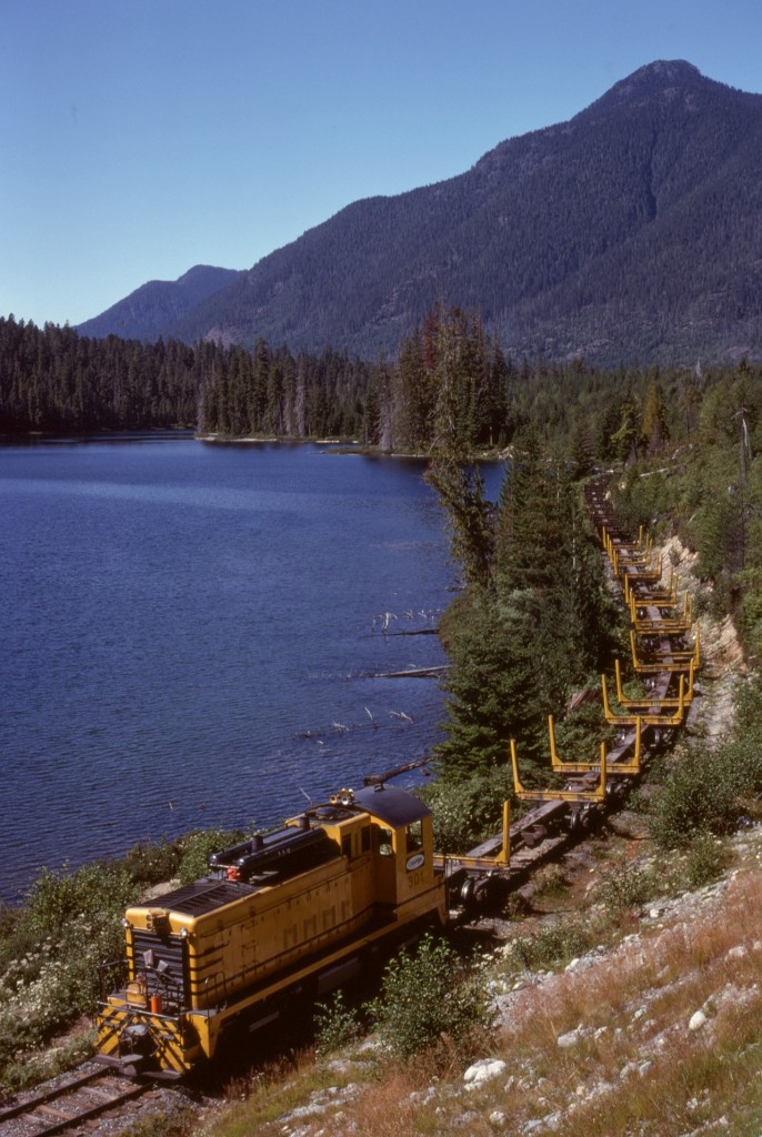 On northern Vancouver Island, Canadian Forest Products had a spur eastward from Woss to a road-to-rail log reload at Crowman Lake (which CFP spelled Croman), passing along the north side of Hoomak Lake around the halfway mark, thus the H-Line name of that spur.  On Wednesday 1979-08-29, dynamic-brake-equipped SW1200 301, new to CFP in 1956, handled a long string of skeleton log empties by Hoomak Lake enroute the Croman reload, with Mount Markusen prominent in the background.

This H-line spur is the same line where a multiple-fatality runaway of loaded log cars occurred closer to Woss on 2017-04-20 (https://www.tsb.gc.ca/eng/rapports-reports/rail/2017/r17v0096/r17v0096.html) which resulted in the total shutdown of that railway (then the Englewood Railway of Western Forest Products) as announced on 2017-11-07.