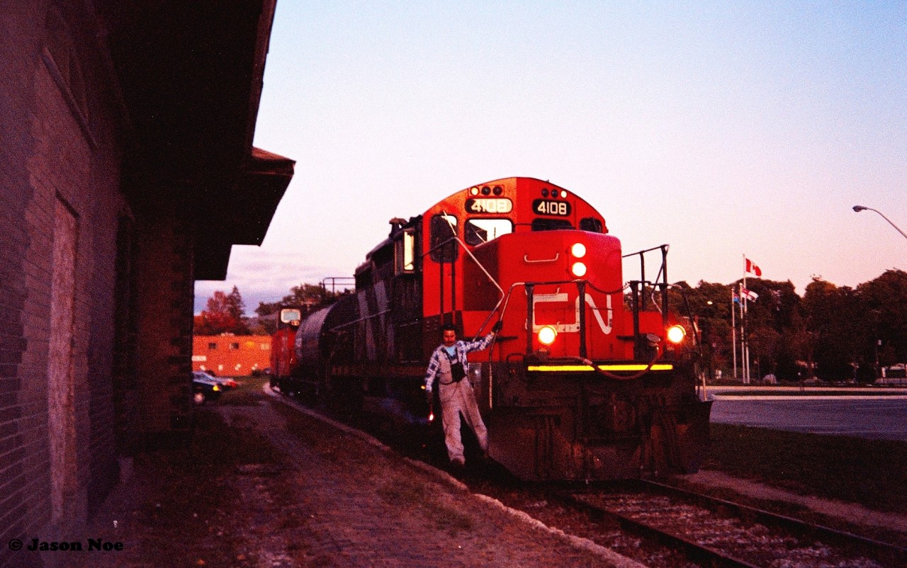 Just as the late September sun has dipped below the horizon, the CN 15:30 Kitchener Job slowly passes the former Grand Trunk station as it approaches Regina Street in downtown Waterloo, Ontario. The job is powered by GP9RM 4108 and is taking one car to Elmira along with caboose 79883.