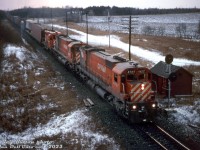 On a gloomy winter's day in December, CP train #904 rolls past the sectonman's shanty at Puslinch on the Galt Sub, lead by M636 4727, M630 4557, and GP30 5000 (one of CP's two GP30 units, and the only two that were Canadian-built by GMD in London). Some open autorack and piggyback traffic follows on the head end.
<br><br>
<i>Reg Button photo, Dan Dell'Unto collection slide.</i>