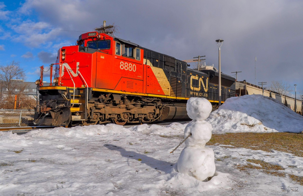 On December 13, 2023, Canadian National EMD SD70M-2 8880 leads train 305. I decided to take an original shot taking advantage of the presence of a snowman, seeming to observe the passing trains.