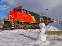 On December 13, 2023, Canadian National EMD SD70M-2 8880 leads train 305. I decided to take an original shot taking advantage of the presence of a snowman, seeming to observe the passing trains.