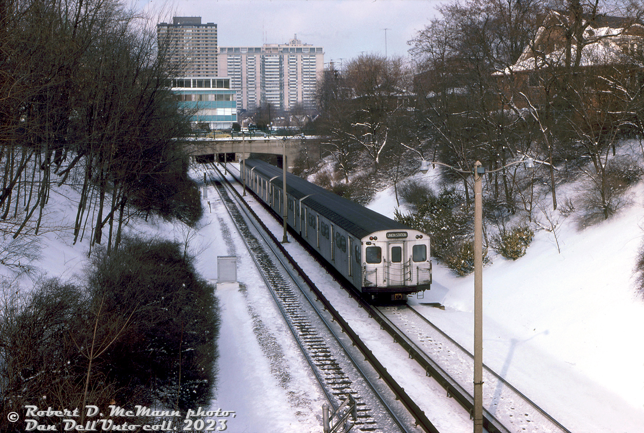 A 4-pack of subway cars with two of TTC's Montreal-build MLW M1's (5300-5335 series, the only MLW order) trail two Hawker Siddeley H-series cars on a northbound Yonge line train in this wintery scene. The consist is passing through the open-cut section of the Yonge Line north of Rosedale Subway Station, passing under Roxborough Street, and about to duck back underground for their stop at Summerhill Subway Station. The green low-rise office building in the background, off Price Street, survived until the early 2020's before behind demolished for redevelopment.

Robert D. McMann photo, Dan Dell'Unto collection slide.