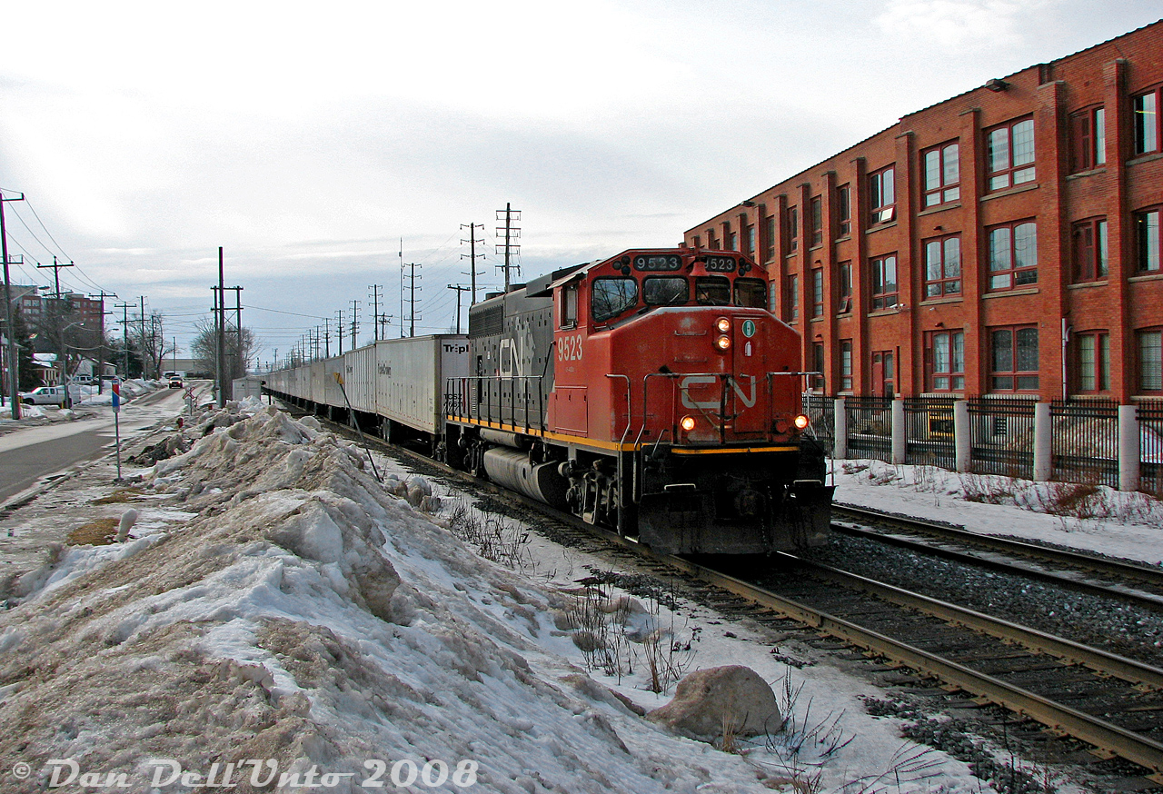 After a trip back from downtown Toronto, a stopover was made in downtown Brampton during the afternoon lull period, before the "GO rush" began. Afternoons on CN could be slow sometimes (maybe passed by a visit to "The Little Train Shoppe" across from the tracks, or Gusto's Pizza nearby), but one of the trains that did show up was the daily eastbound Roadrailer (CN train #144), that typically got a single 4- or 6-axle, often an older unit such as a GP40 or SD40 variant. The westbound counterpart (#145, except Friday as #147) was usually an evening train after the GO rush.

Today, we have CN GP40-2L(W) 9523 (fading paint) leading eastbound Roadrailer train #144 through downtown Brampton. The trailers are busy hammering away at the CN-OBRY (ex-CP) diamond with the Owen Sound Spur, as 9523 is just about to pass Mill Street crossing and the nearby station. Snowbanks piled up along Railroad Street often provided a good vantage point, as this area was usually weeded out in the warmer months.

The last CN-NS Triple Crown Roadrailer trains would run in November 2015.