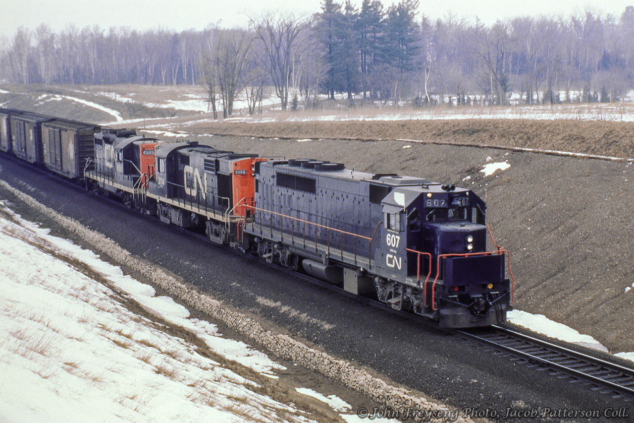 A westbound extra descends the grade along the Halton Sub just west of mile 30 at side road 10.  Evidence of recent upgrades can be seen in the surrounding landscape as the former Milton Subdivision branch line became CN's westerly mainline out of the GTA.  Leading the train today is GO Transit GP40TC 607, the highest numbered of eight units numbered 600 through 607, which were broken in hauling CN freight trains over the course of a few months. The units would have their paintjobs modified to official GO Transit colours by April 1967 for final equipment testing before the start of service on Tuesday, May 23, 1967.John Freyseng Photo, Jacob Patterson Collection.