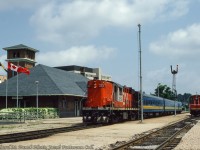 VIA Rail train 663 behind leased CN Tempo RS18m 3153 makes its stop at Guelph on a warm summer day.  The Tempo units only had about a year left in service before retirement in 1983.  At right is CN 7242, power for the Guelph yard job.<br><br><i>Richard M. Panek Photo, Jacob Patterson Collection Slide.</i>