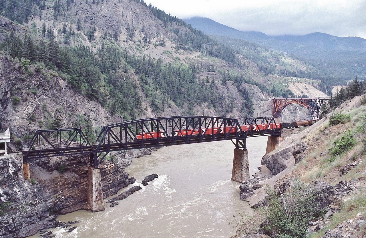 The bridges  of  Cisco.


   The Multi-Mark is alive and well.


   And SD40's ruled


   Westbound on CP Rail, near (what remains of) Lytton, B.C., May 13, 1980 Kodachrome by S.Danko


   Noteworthy: The Kodachrome was exposed prior to the directional running co-operation agreement: 


   Currently the  CP line  is eastbound, CN line is  westbound (Executive and Business Trains excepted).


   Engineering: for those that need to know, from Wikipedia


  The Canadian National bridge is a truss arch bridge, 247 metres (810 ft) long and 67 metres (220 ft) high. The north-west end of the bridge abuts into a near-vertical rock face. The south-east end of the bridge crosses the CPR tracks about 100 metres (330 ft) north of the CPR bridge. 


The Canadian Pacific bridge is a 3-span, 160-metre-long (520 ft) truss bridge. There are two short Pratt truss spans at each end of the longer Parker truss main span. The south end of the bridge (on the west bank of the river) enters directly into the Cantilever Bar Tunnel, in the side of the Cisco Bluff. 



The original span was built by Joseph Tomlinson and was pre-fabricated in England and shipped to Canada in 1883.The bridge – then one of the longest cantilever spans in North America – was then constructed by the San Francisco Bridge Company. When the current bridge was built at Cisco in 1910, the original span was moved to the Esquimalt and Nanaimo Railway on Vancouver Island to cross the Niagara Creek Canyon (48.4825°N 123.5574°W), where it is still in use (now by the Southern Railway of Vancouver Island). 


sdfourty
