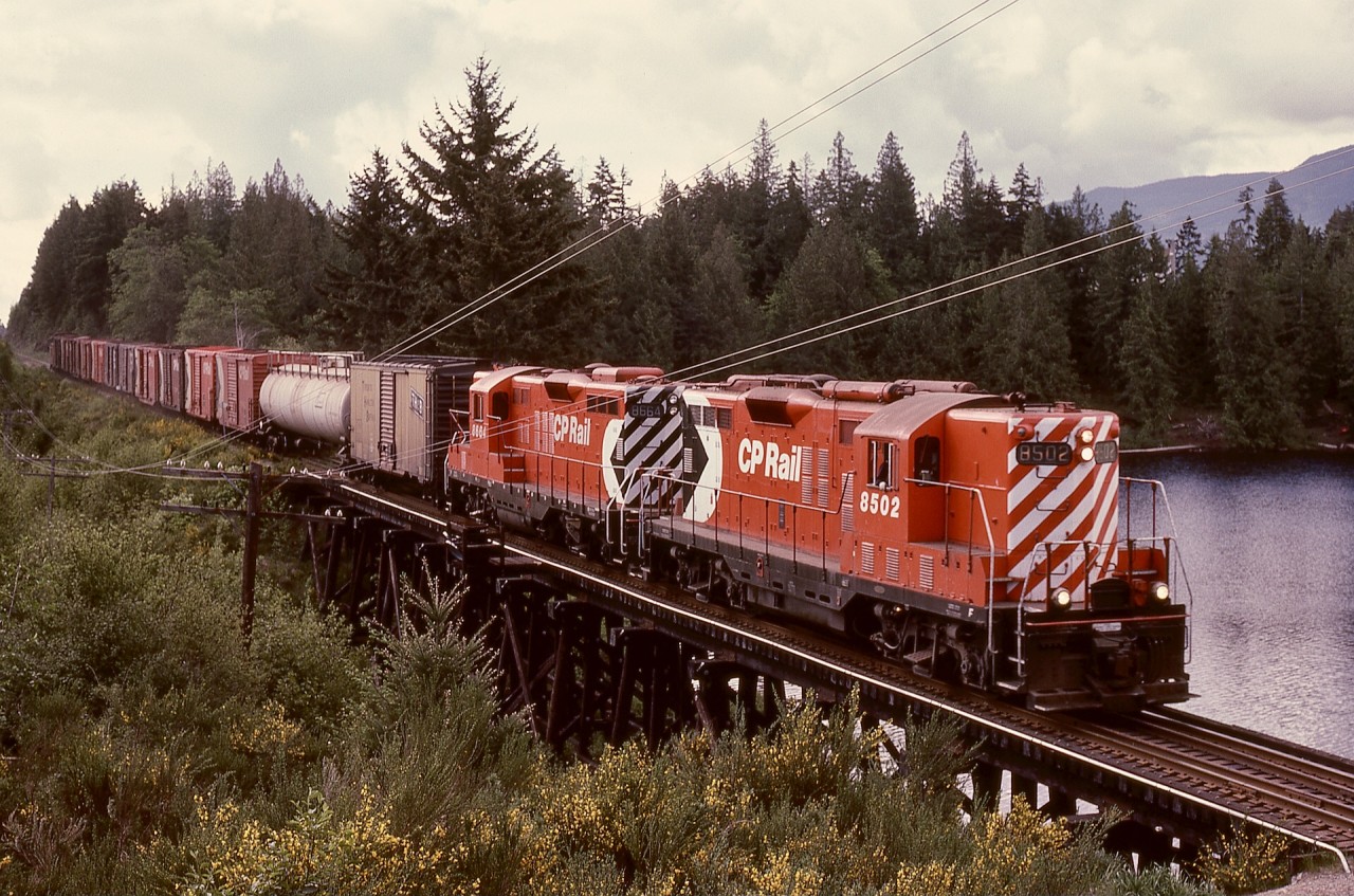 North of Wellington and at mileage 79.9, CP’s Victoria subdivision had a pile trestle bridge over an arm of Green Lake, and on Wednesday 1979-05-16, that was traversed by freight train No. 71 with GP9s CP 8502 and 8664 at 0941 PDT enroute Port Alberni.  The rooftop air reservoirs on 8502 indicate its origin as a steam generator equipped unit.

Note the handy comparison of multimarks, original full-height on 8502 and newer smaller one on 8664.