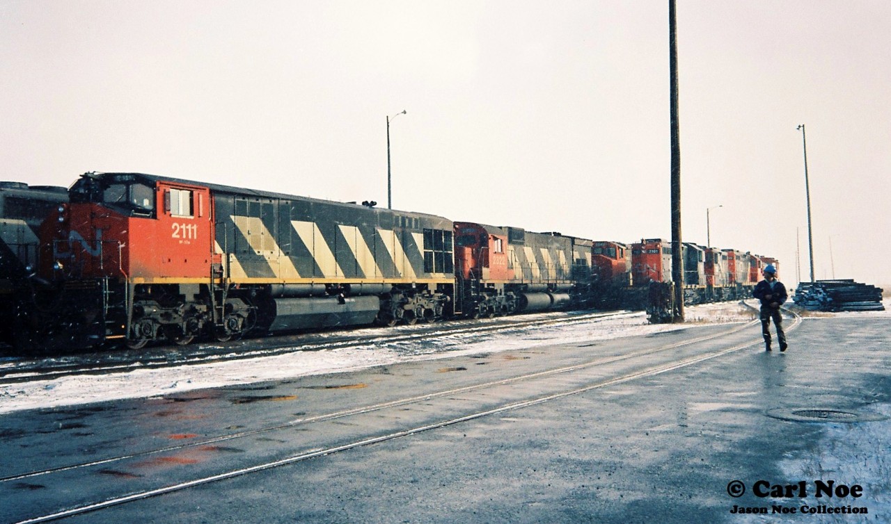 During an early winter snow squall, various units are seen crowding the CN MacMillan Yard diesel facility tracks in Vaughan, Ontario. HR-616 2111 with M-636 2322 await their next assignment along a set of local power that includes CN SW1200RM 7101. To the right, future railpictures.ca contributor Andy Gertz (with an Operations Exploration hardhat) looks on; no doubt ready to capture his next frame of Kodachrome 64.
