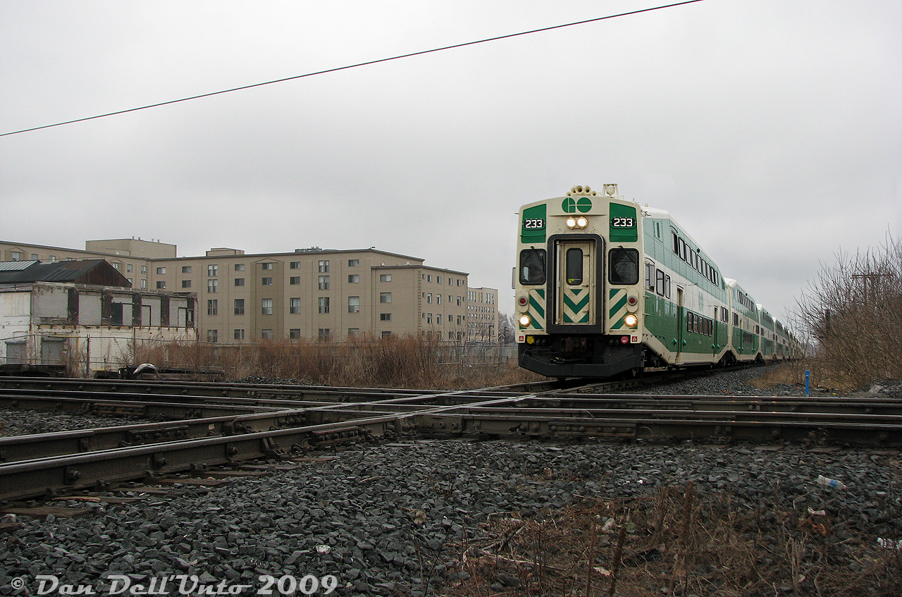GO Transit cab car 233 leads train #801, the first northbound Barrie line train of the PM rush hour parade, northbound up the CN Newmarket Subdivision, about to slam the Davenport diamond interlocking plant with CP's North Toronto Sub, just north of Dupont Avenue.

The gentrification is strong in this former industrial bastion of Toronto: the tan building in the background is the old American Standard plant (manufacturer of sanitary products like toilets), that had been converted into lofts. On the left was the old Canadian General Electric (CGE) Royce Works plant at Dupont and Lansdowne (Dupont used to be called Royce Street). Most of the plant, once spanning that entire southwest quadrant of the diamond, had been demolished. The original building at the corner was spared, and incorporated into the new condos later built on site. There was once a connecting track between CN and CP here, used for interchange and accessing some of the local aforementioned industries. On the northeast quadrant (out of frame) was the old CGE Davenport Works, partially converted into lofts and housing (the north headhouse had been converted, the south headhouse was eventually demolished).

Davenport would continue to see GO bilevels clatter over the diamond until April 2023, when the new grade separation opened under Metrolinx ownership. A concrete flyover and more condos greets anyone standing in this spot today.