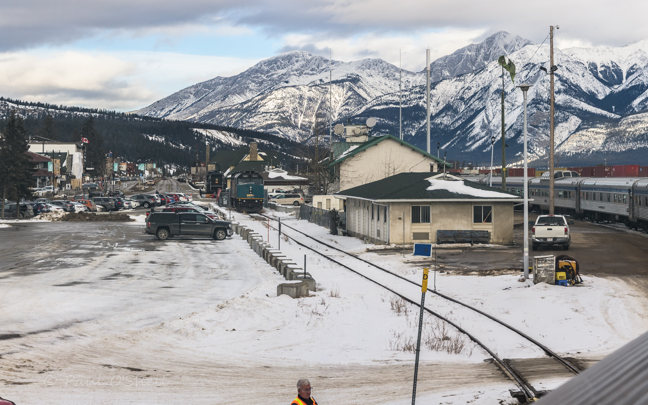 Steam, Diesel, Passenger & Freight  
VIA #2 The Canadian winds its way into Jasper, AB Mile 0.0 CN Albreda Sub. on January 27, 2024 with a plethora of railroad equipment all around. 
CN 6015 sits on static display in the distance near the iconic VIA Rail station, while VIA 6421 sits on the team track waiting its turn to pull The Skeena, or possibly be added to the consist of a west bound Canadian. Double stack hot shots fill the yard waiting for new crews on both east and west bound trips. 
At the bottom center of the frame a VIA Rail Car knocker does a visual inspection of the equipment on The Canadian as it eases into the platform area. 
The CN windsock shows the steady, but pleasant breeze that was awaiting me when I stepped off the train for a walk around town before continuing my eastbound journey to Toronto.
