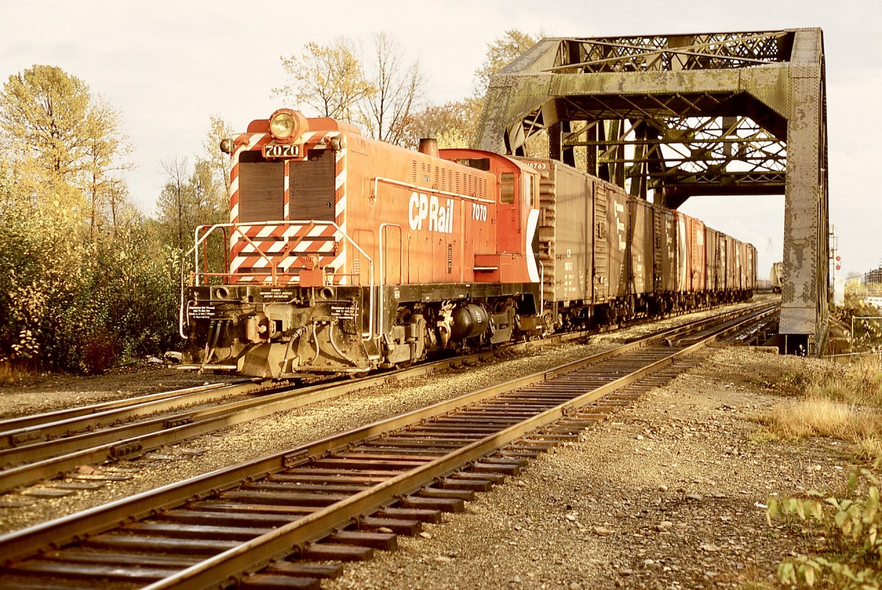 The west end of CP’s Coquitlam Yard (always in the City of Port Coquitlam, how logical!) was marked by a two-track through steel truss bridge over the Coquitlam River.  Here, on Wednesday 1972-11-04, Baldwin switcher 7070 (an engine I came to know well six years later on Vancouver Island) is wearing a fairly fresh coat of paint and is busy sorting a string of cars, at a then nameless location previously (before 1928) Westminster Junction and later (1988) MacAulay.  That bridge continues to serve to this day.