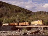 Southward from Woss on Vancouver Island, Canadian Forest Products crossed Maquilla Creek at milepost 50 (visible at the end of the tank car), just before Maquilla Reload.  On Monday 1975-06-09, CFP 302 had two loads of ties and a tank car in addition to a string of log empties southbound, in the era before better highways reduced the need for company camp supplies to be transported by rail.
