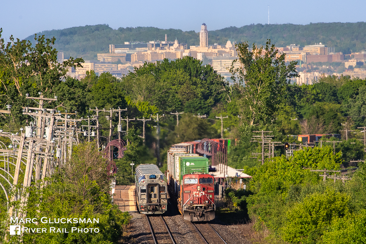 Smokin' Montreal Meet. On the afternoon of May 29, 2023, CPKC Canadian Pacific Train 112 with CP 8858 (ES44AC) as the outward facing DPU passes EXO Train 25, a Line 11/Vaudreuil bound 6-car train led by EXO 3003 at the Point-Claire Station in Montreal Quebec on warm afternoon of Monday, May 29, 2023. Some 10 miles (about 16 km) behind the trains in the background the 269 foot (82 meter) tall Roger-Gaudry Building at The University Of Montreal rises above the tree line. This is a great area to spend the rush hour as it is extremely busy for train traffic with EXO, VIA, CPKC, and CN all passing with good frequency.