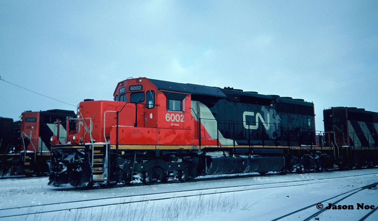 1994 was such an awesome year for railfanning. As my world of train photography widened from Kitchener and my hometown Waterloo Spur, I soon saw that there was so much going on with both CN and CP motive power rosters. As well, each railway was attempting to change their corporate images and were quickly repainting units in new schemes as fast as their paint shops would allow.  As the history books would note, both the CNNA scheme and CP Rail duel flags scheme would dissipate without any fanfare and the railway’s would later eventually try to go back to their roots to salvage cooperate images. However that was all bigger picture stuff. As my notes indicated 30 years later, there was no better place to start my memories of 1994 than at Kentucky Fried Chicken, no abbreviations, as that’s actually what it was called at that time. 

Andy Gertz’s scanner crackled to life as we were waiting for our lunch inside the restaurant. CN 5100 east was coming towards London on the Strathroy Subdivision from Komoka. With several very fresh two and three piece combos now in hand, my dad drove us towards the CN yard as it was learned that this eastbound was going to lift two units at London East. Pictured here, CN SD40 5100 and SD40u 6002 are at London East with CN GP9RM’s 4135 and 7037 in the background.

 According to my notes, both GP9RM’s had recently returned on a local job from St. Thomas. CN 6002 was rebuilt from SD40 5118 the year prior by AMF in Point Ste. Charles, Quebec and was freshly adorned in the CNNA paint scheme.