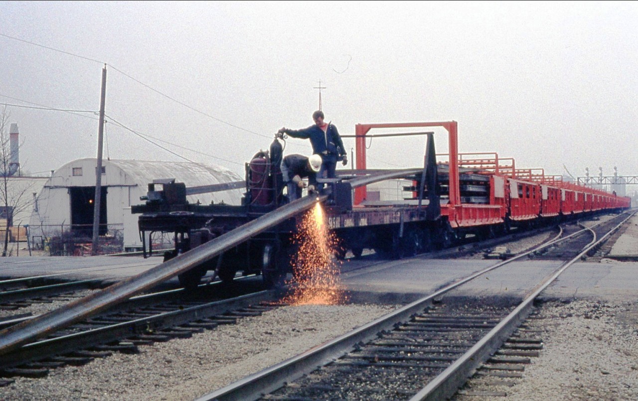 I'm not sure if I would be looking on if one was using a torch to cut the CW Rail without safety glasses but that's how it back in this 1977 photo. Here's a CNR CWR train laying rail at Chartwell street as the conductor looks on with his lunch box radio, waiting to pull the movement westward and to start dropping the rail clear of the crossing. Taken from my fathers collection.