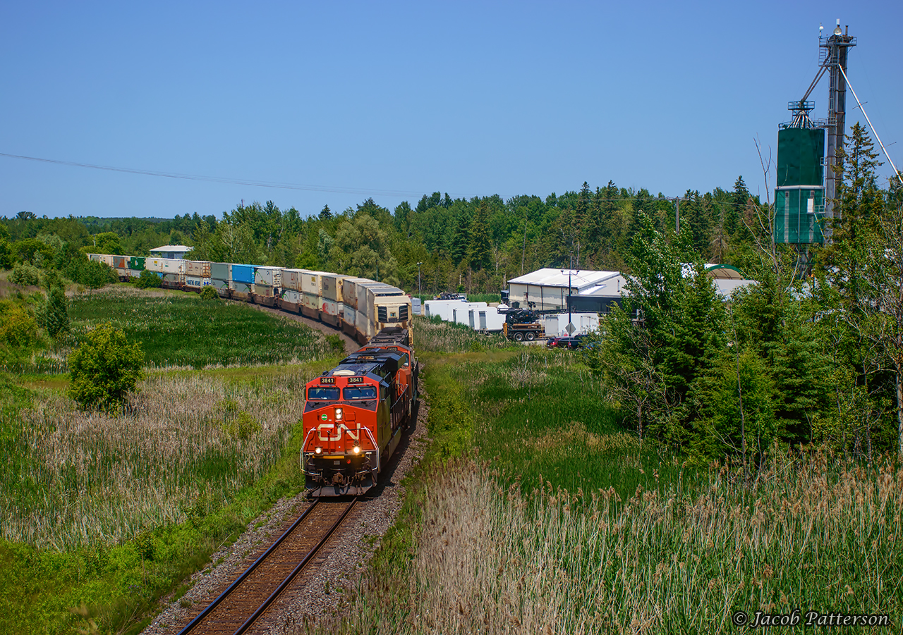 After meeting 105 at Zephyr, CN 104 gets up to track speed through the curve at Mount Albert.  At one time a town served by two railways, today the CN Bala Sub, originally built by the Canadian Northern in 1906, sees all traffic on its transcontinental journey.The other line, arriving in Mount Albert in 1877, was the narrow gauge Lake Simcoe Junction Railway, a subsidiary of the Toronto & Nipissing Railway. The LSJR was constructed from Stouffville Junction to Jackson's Point on Lake Simcoe via Ballantrae, Mount Albert, and Sutton, eventually crossing the Canadian Northern at Zephyr, just north of Queensville Sideroad.  Traffic levels dwindled after the construction of both the CNoR, and the Toronto & York Radial Railway to Sutton (opening 1909), resulting in the abandonment of the Sutton Sub between Zephyr and Stouffville Junction in 1928 (service ending in May, and rails lifted by October).  Jackson's Point to Sutton had been abandoned in 1927.  Redesignated as the CN Sutton Spur in 1960, service would cease in 1979, with the rails being lifted in 1981.  The LSJR passed roughly 1000 feet off to the right of this image.Some information can be found on the late Charles Cooper's website by clicking here, and further information can be found in his book Narrow Gauge for Us: The Story of the Toronto & Nipissing Railway.

Scenes of Mount Albert station, relocated to Cannington, ON in 1978:
September 1976, Arnold Mooney
March 1978, Arnold Mooney
Fall 1978, Peter Newman

Scenes of CN's Sutton station, relocated to Georgina, ON in the late 70s:
October 1976, Arnold Mooney
October 1976, Arnold Mooney