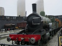 London and Southwestern Railway 4-4-0 number 563 and a coach rest on the turntable at the John Street roundhouse. The equipment was brought over from England for the theatre production of "The Railway Children". During shows the train was moved into the stage area by a trackmobile. The production was not very successful and the equipment was returned to England. The locomotive was restored to operation in 2023. The engine probably felt at home on this grey misty day.