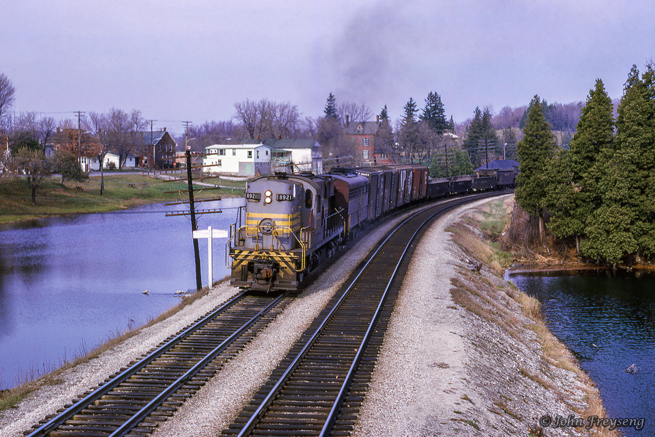 The climb up the Niagara Escarpment almost complete, extra 8921 west rounds the curve at Campbellville passing the famed ponds, a setting for many rail photographers through the years.  Note the roof of the Campbellville station just above the open top hopper in the distance.Scan and editing by Jacob Patterson.

See this train earlier at:
Hornby
Christie

More Campbellville Ponds:
August 1959 by Willa Thomson
Summer 1978 by Bill Thomson
June 1997 by Arnold Mooney