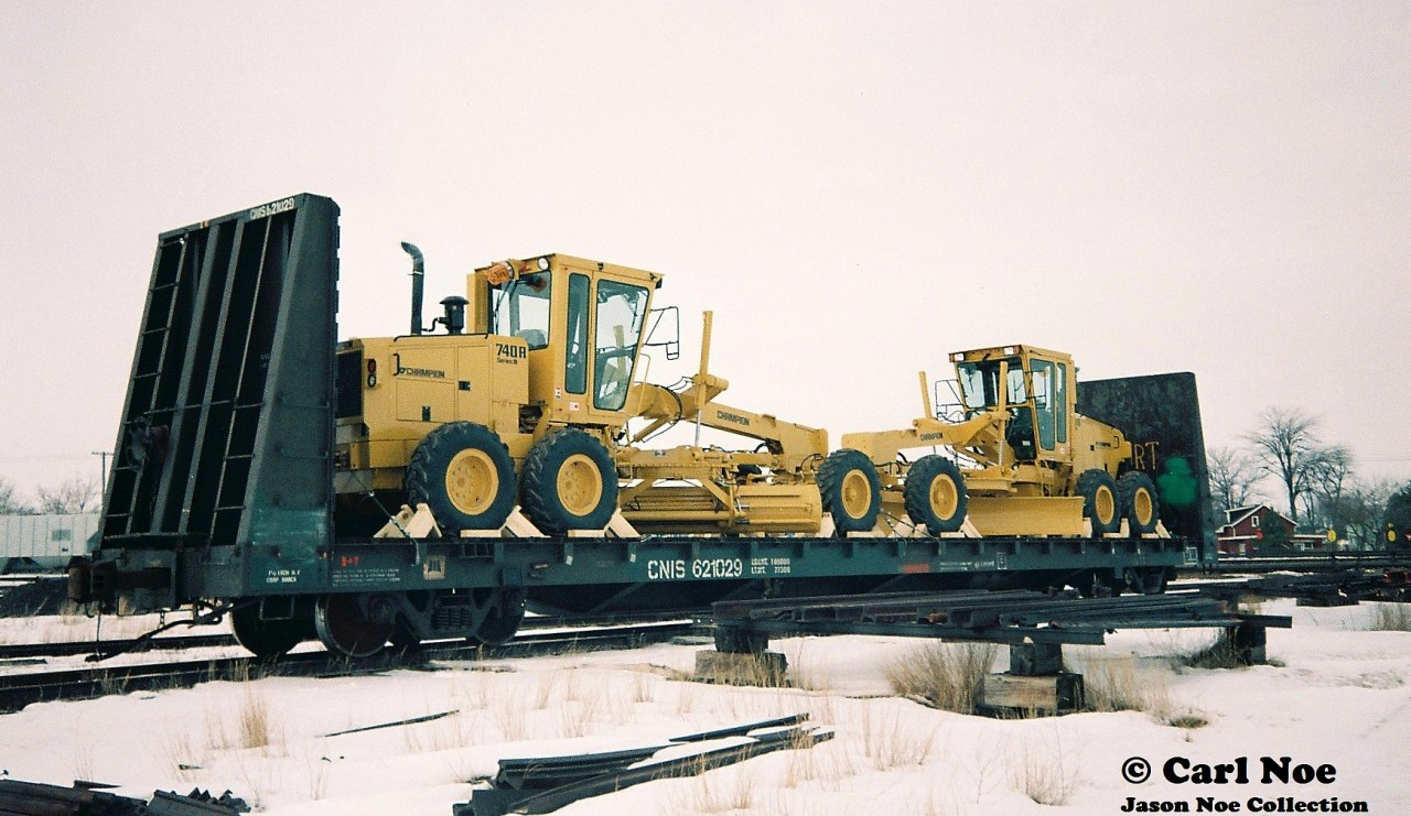 A CN bulkhead flatcar loaded with brand new Champion road graders is seen at the CN yard in Stratford, Ontario on February 6, 1994. Presumably, it will eventually be lifted by either CN 421 or 422 to continue its journey. The new equipment was brought down from Goderich via the Goderich-Exeter Railway after being lifted from the Champion Road Machinery plant in the town. 
In 1997 Volvo had paid $173-million to take over Champion Road Machinery. However, in 2008 it was announced they were going to close the road grader plant by 2010, eliminating 500 jobs, and consolidating its road machinery operations in Pennsylvania. At the time, Volvo had said this move was made to improve competitiveness and profitability while reducing exchange rate fluctuations as our Canadian dollar had risen incredibly high.