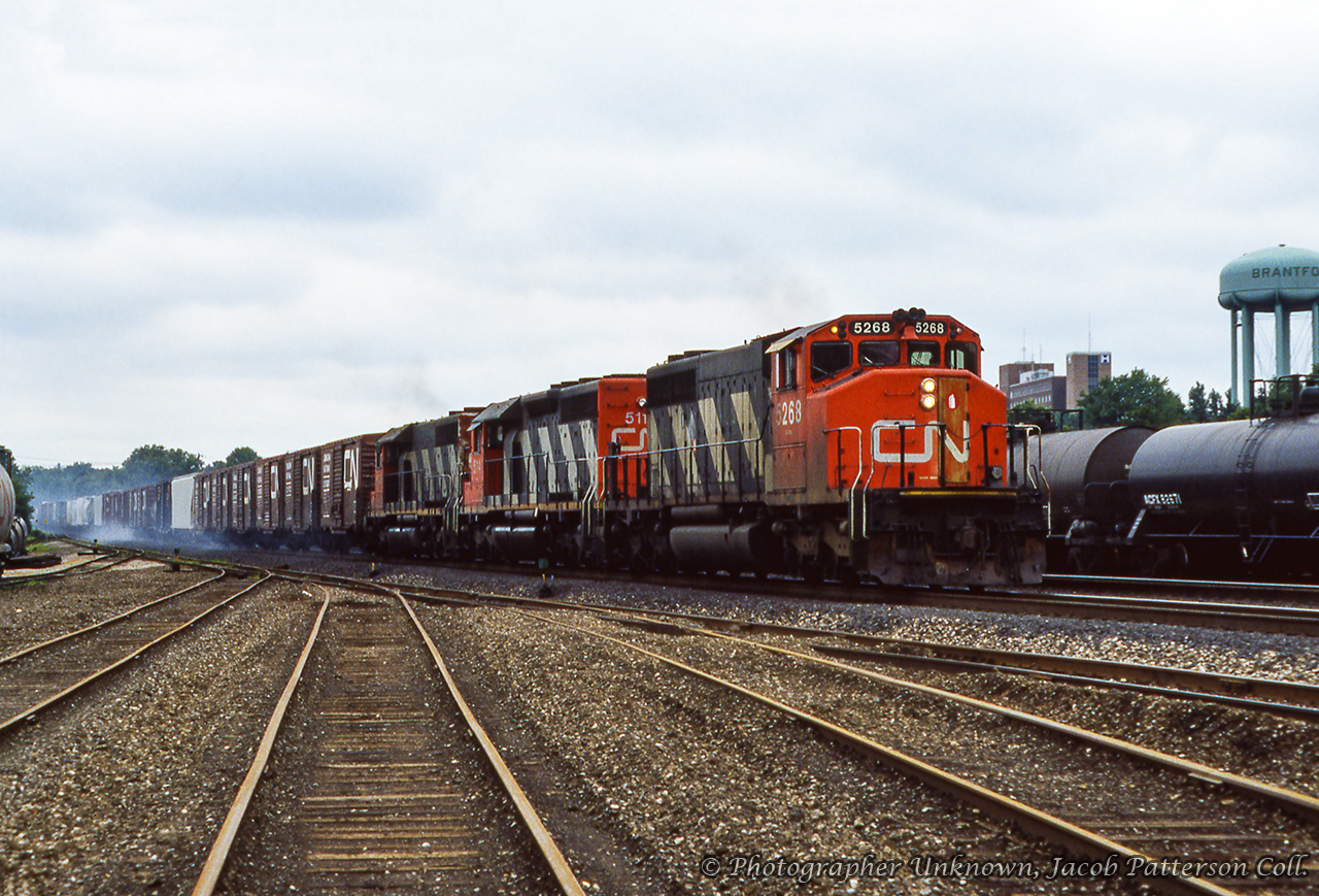 Brake shoe smoke swirls around trailing freight cars as a trio of GMD SD40 variants roll an eastbound extra into Brantford.Original Photographer Unknown, Jacob Patterson Collection.