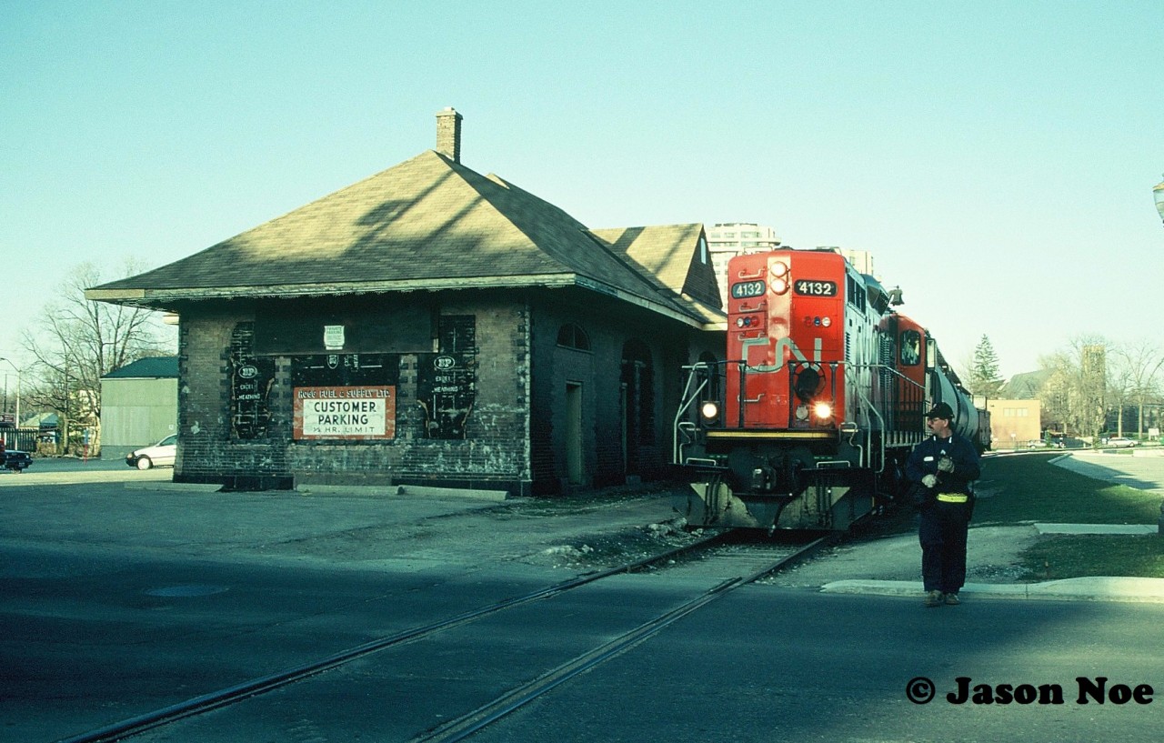 Spring has sprung as CN GP9RM 4132 leads the 15:30 Kitchener Job through downtown Waterloo, Ontario on the Waterloo Spur as the crew prepares to protect Regina Street. The job has three hoppers for Nutrite in Elmira.
